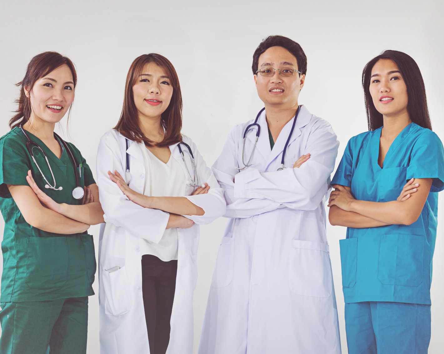 Four medical professionals with confident postures: two women in white lab coats, a man in a white lab coat, and a woman in blue scrubs, all standing against a white background