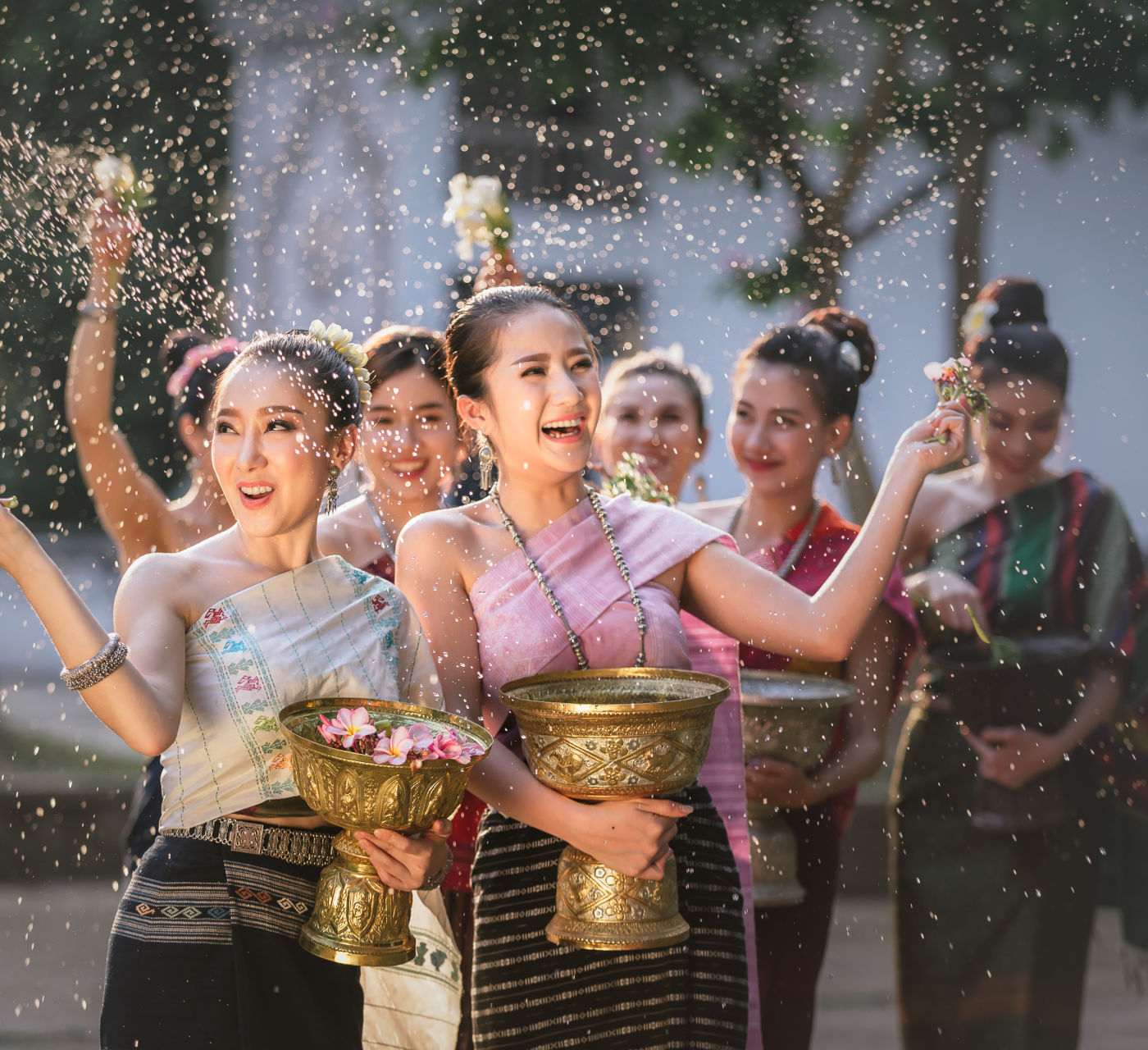 Group of joyful Thai women in traditional attire throwing water during a celebration, with a blurred background