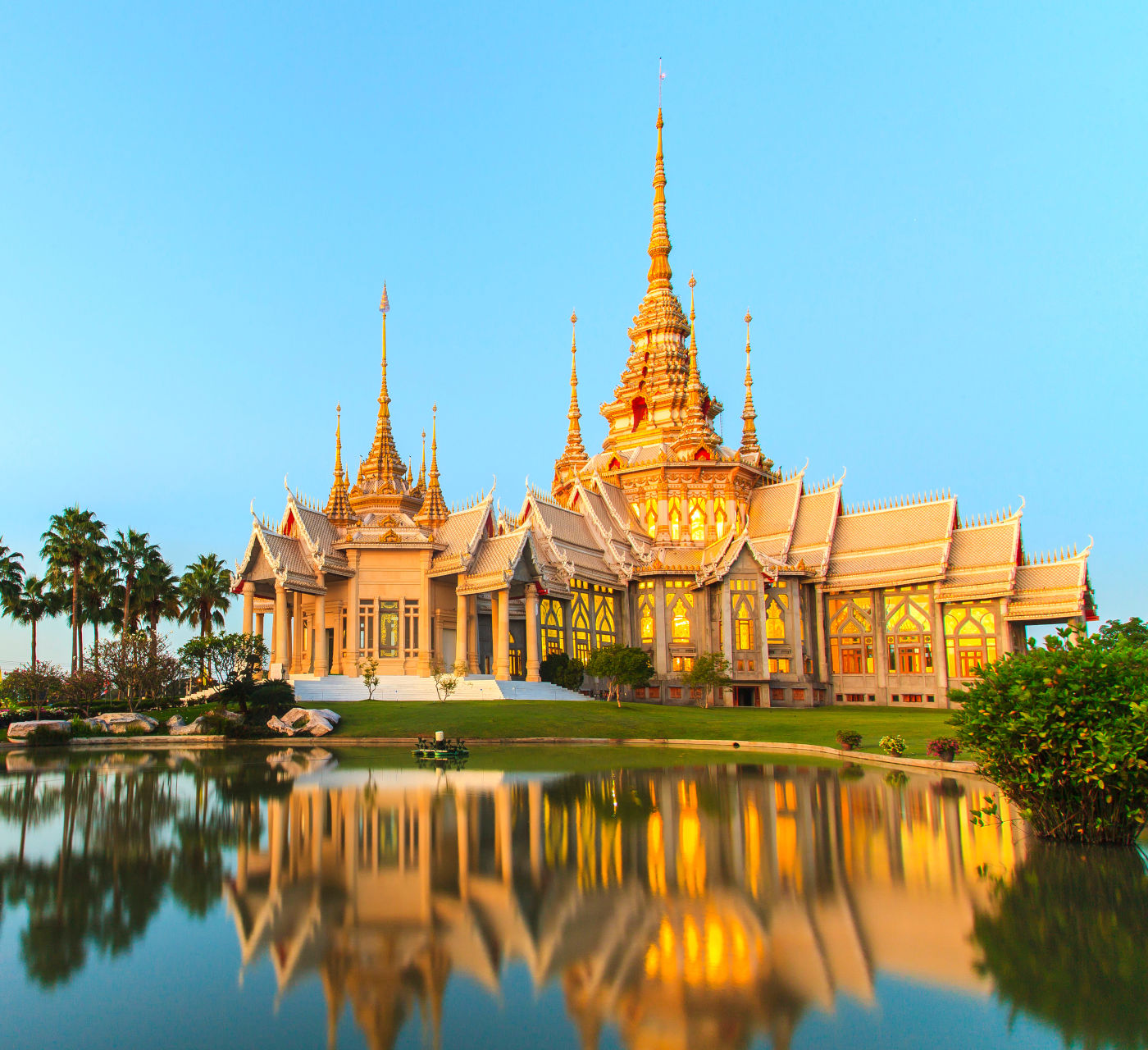 A majestic Thai temple with golden spires and traditional architecture reflected in the water at sunset