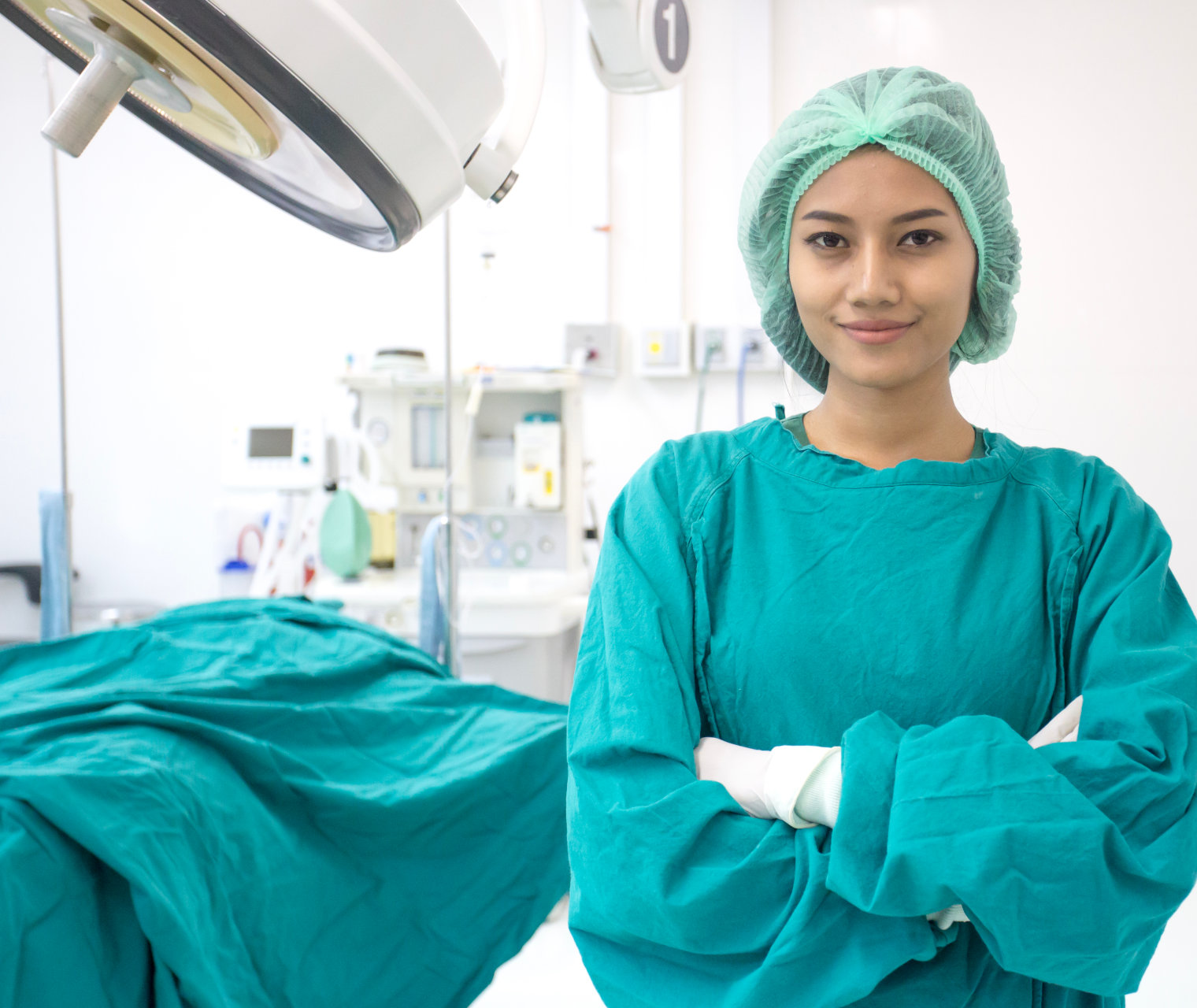 Confident young female surgeon in a green scrub suit with head cap standing in an operating room