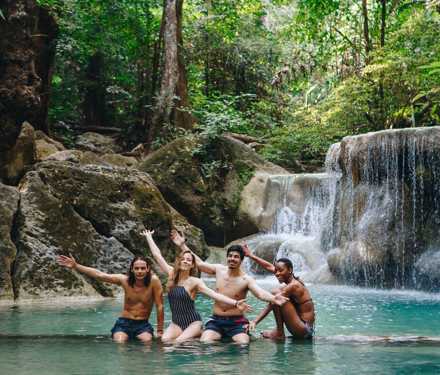 Group of joyful friends enjoying a swim at a natural waterfall in a lush Thai forest