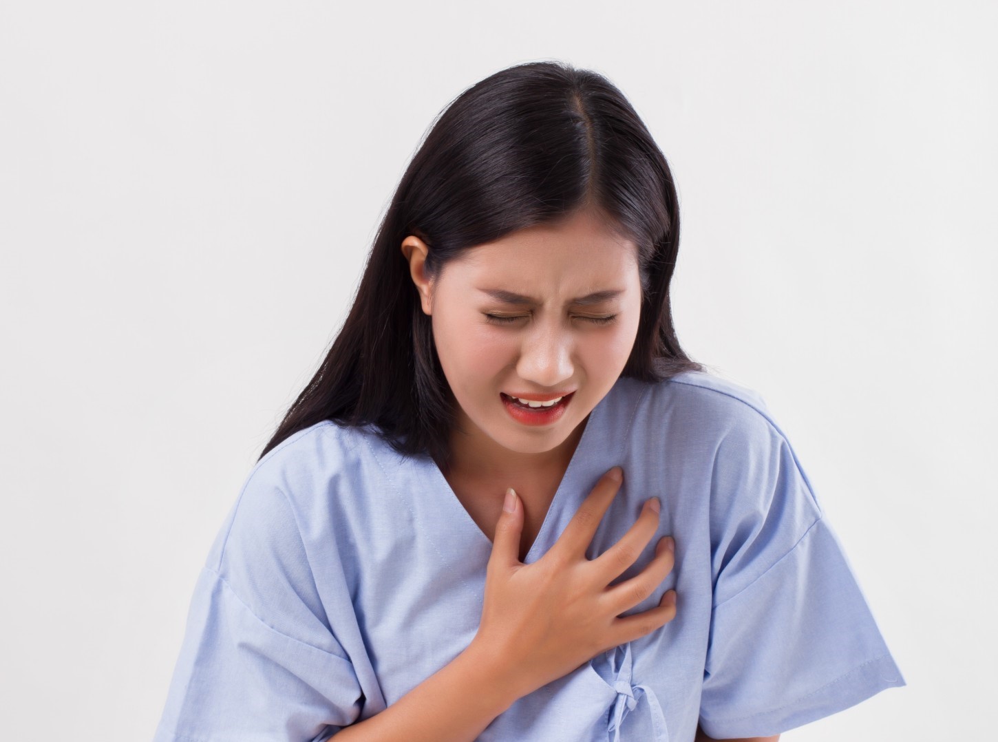 Young woman in a hospital gown clutching her chest in pain