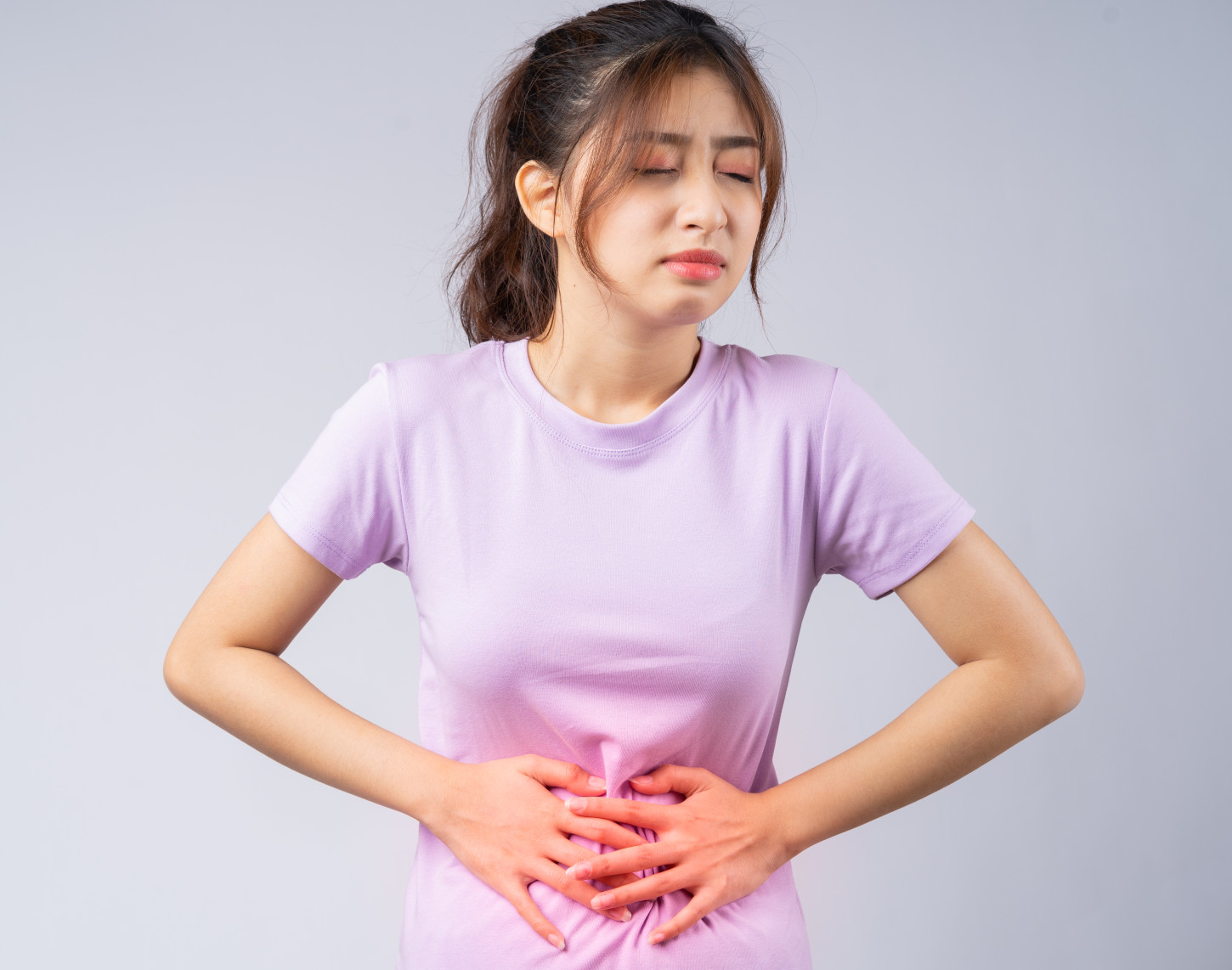 Young woman in purple t-shirt grimacing in pain, holding her abdomen