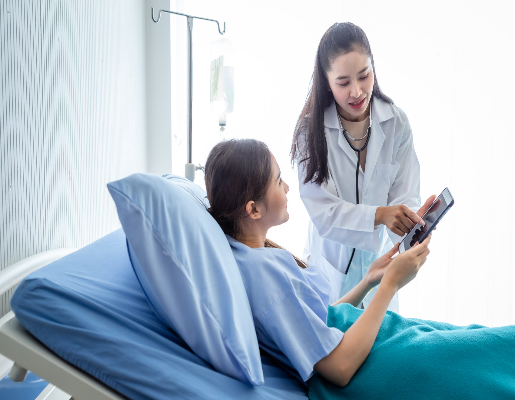 Female doctor showing information on a tablet to a female patient in a hospital bed